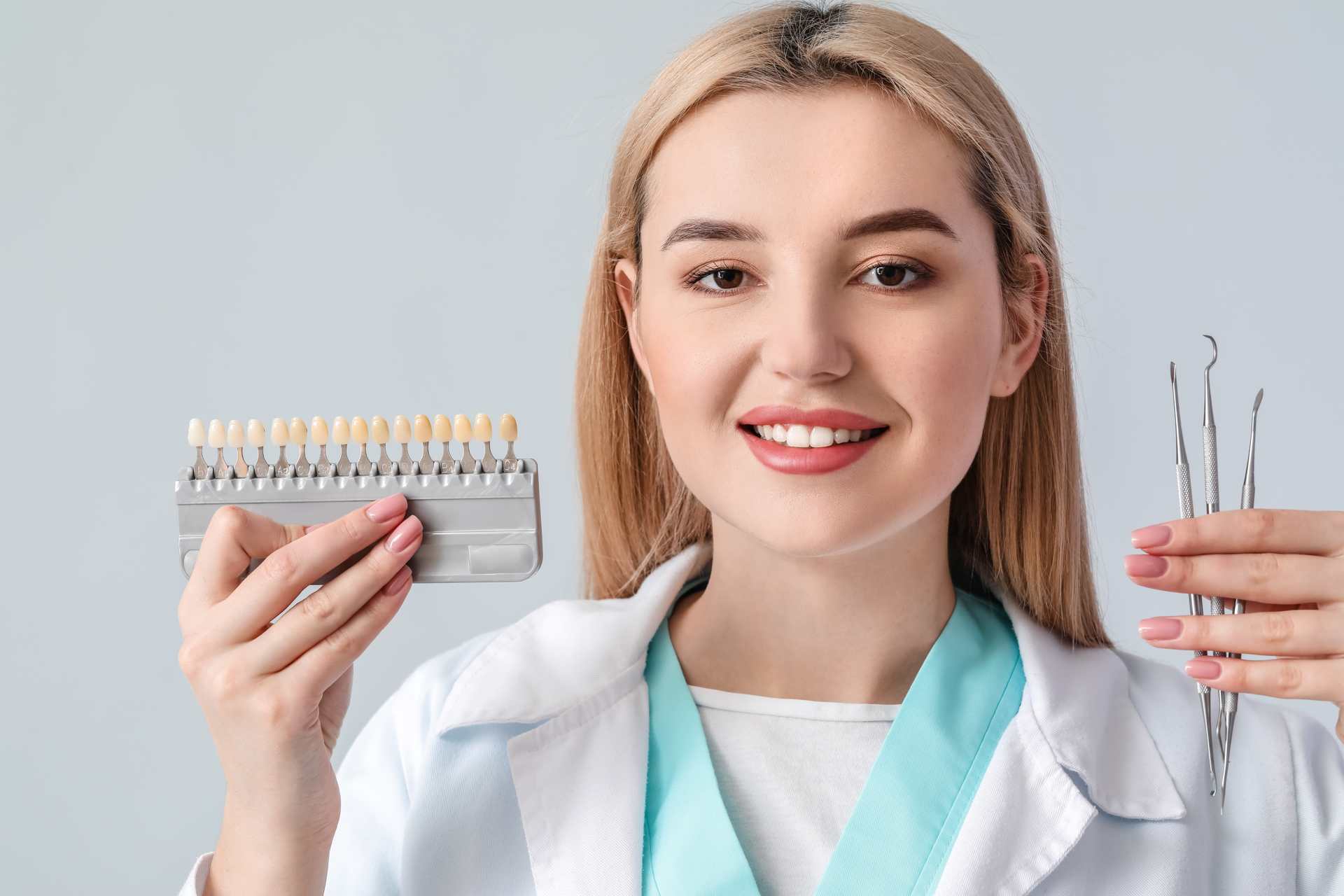 01 A young female dentist on a neutral background holding dentist tools and several tooth samples.