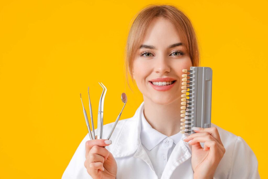 02 Young female dentist on yellow-orange background holding dentist tools and several tooth samples