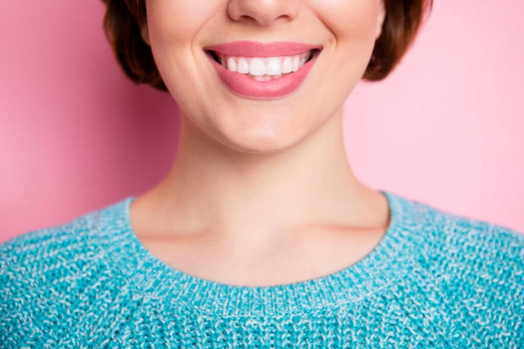 03 Detail of a young woman's radiant smile on a pink background.