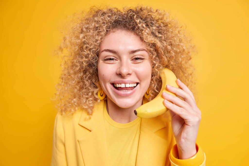 05 A smiling girl with a banana in her hand on a bright yellow background