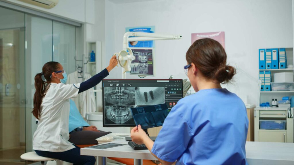 09 Nurse examining a patient's x-rays while the dentist attends to the patient_Lumineers vs. porcelain veneers