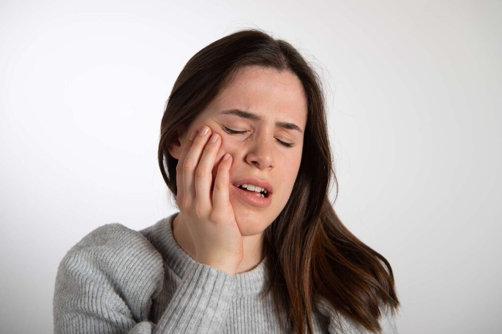 06 A woman with toothache isolated on a light gray background_What is the risk of dental implants_Dental implants pros and cons