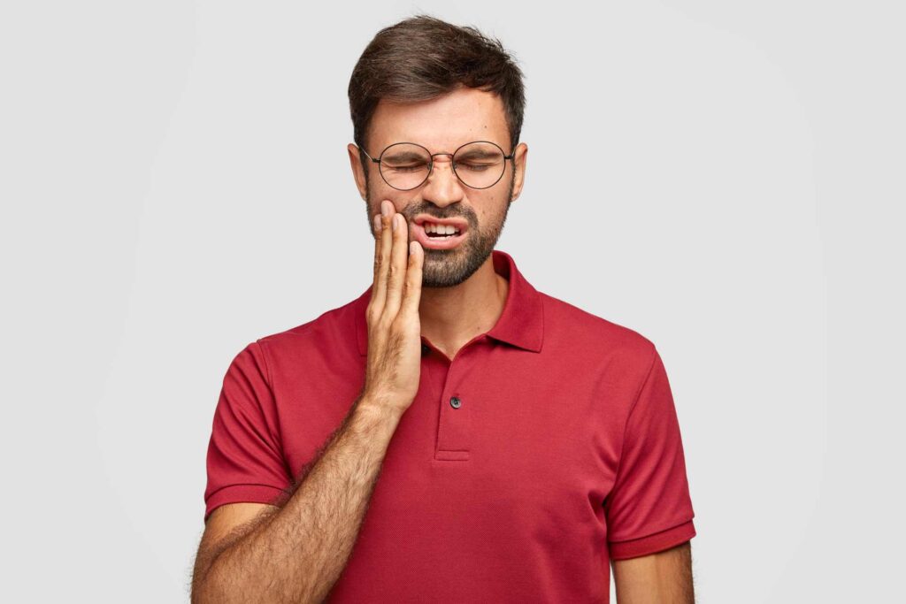 09 Man in dark red T-shirt and glasses feels toothache_Do dental implants hurt