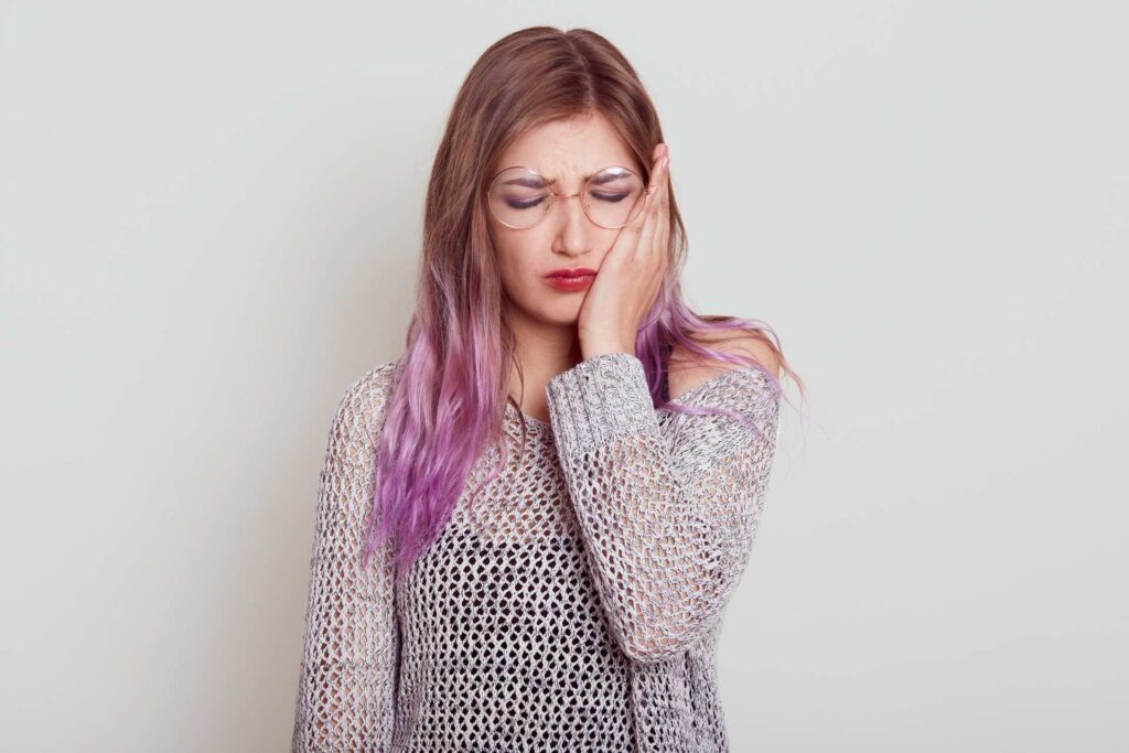 Woman with lilac hair and round glasses, hand on cheek for toothache_tooth