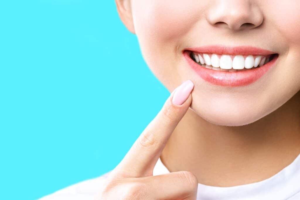 Young woman pointing to her own smile on aqua background_tooth